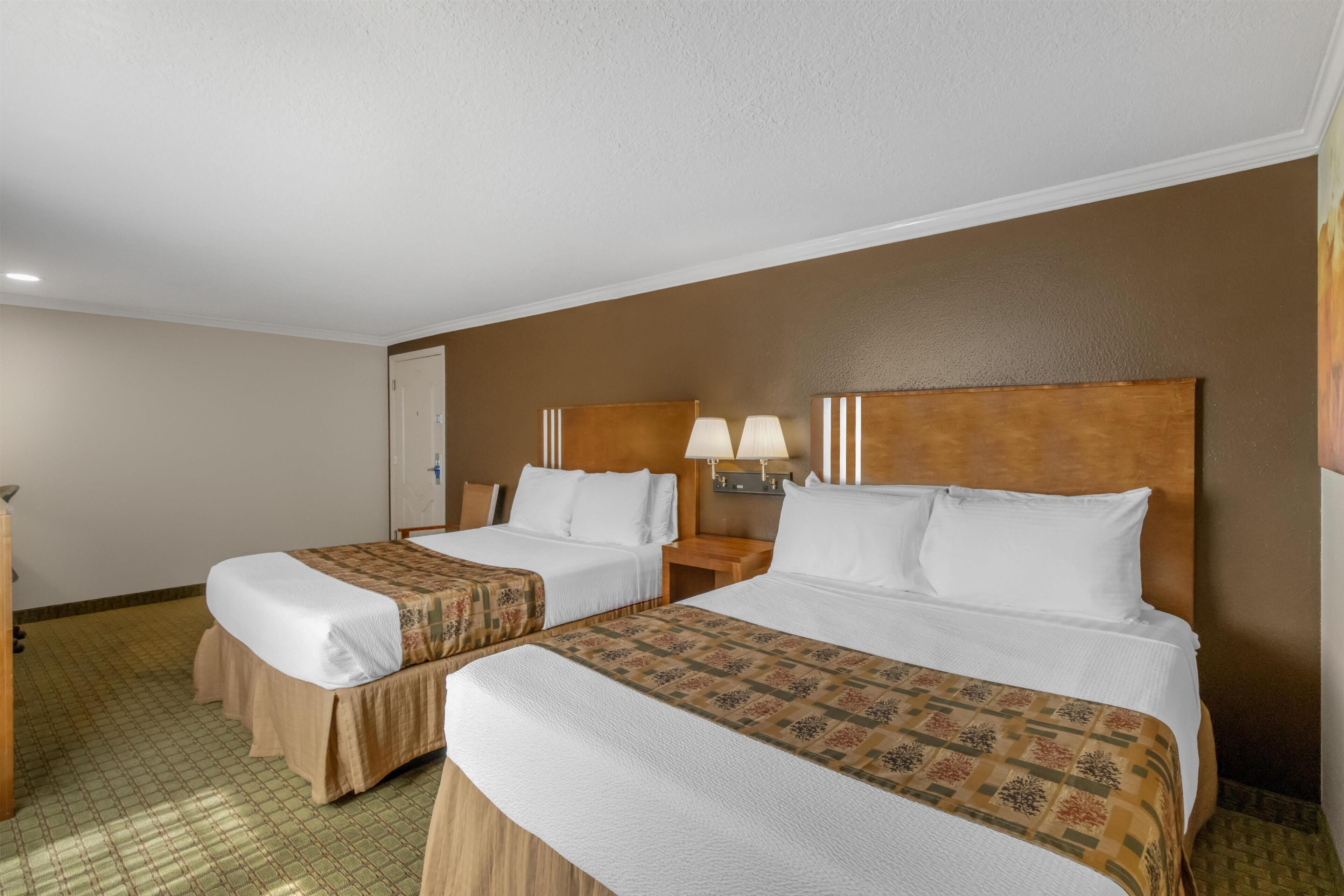 A hotel room with two beds, a nightstand with lamps, and a door.