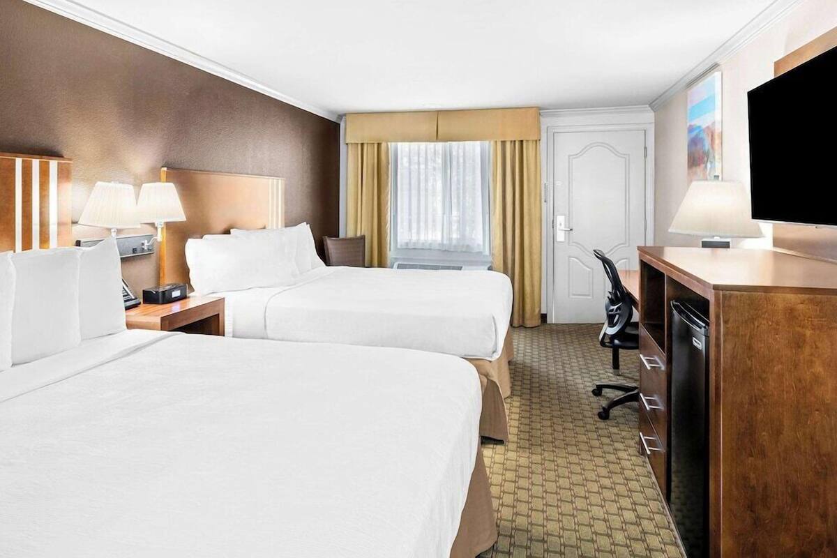 A hotel room with two beds, a desk, a chair, a TV, and a window with curtains.