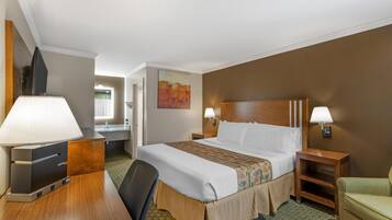 A hotel room with a bed, bedside lamps, a desk with a lamp, a chair, and a painting on the wall.