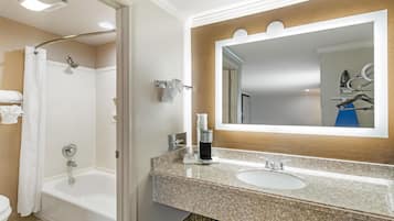 Un baño con ducha, inodoro, lavamanos y un espejo con barra para toallas.