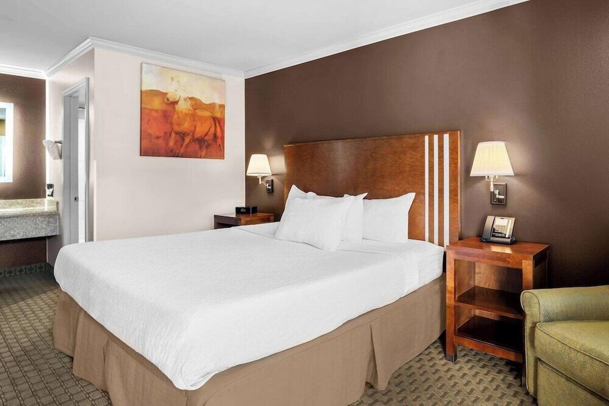 A hotel room with a large bed, two bedside tables with lamps, a painting on the wall, and a green armchair.