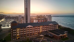 Un hotel moderno de gran altura, ubicado junto a la costa con un puerto deportivo al frente.