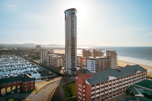 Un hotel costero con un puerto deportivo, una torre alta y vistas a la playa.
