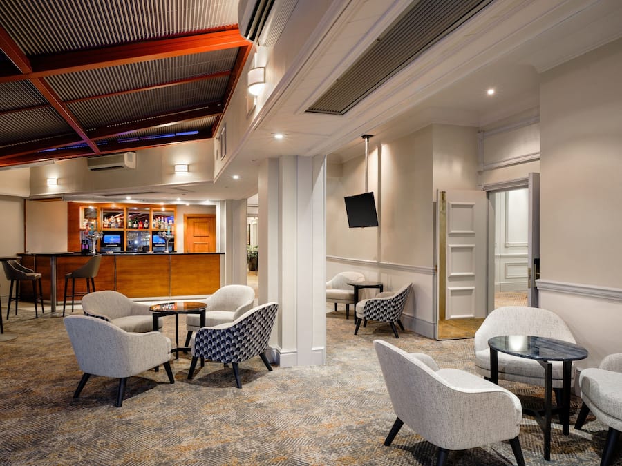 A hotel lobby with a bar area, seating arrangements, and a television mounted on the wall.