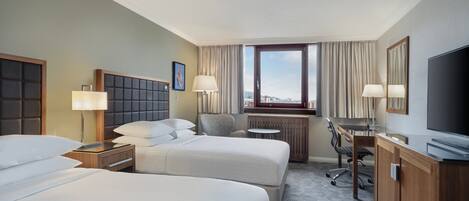 Habitación de hotel con dos camas, un escritorio, una silla, un televisor y una ventana con cortinas.