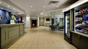 Un vestíbulo de hotel con mostrador de recepción, chimenea, zona de comedor y un espacio para comida para llevar.