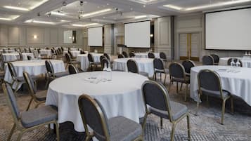 A conference room with multiple round tables, each with chairs, equipped with water bottles and glasses, and a projector screen.
