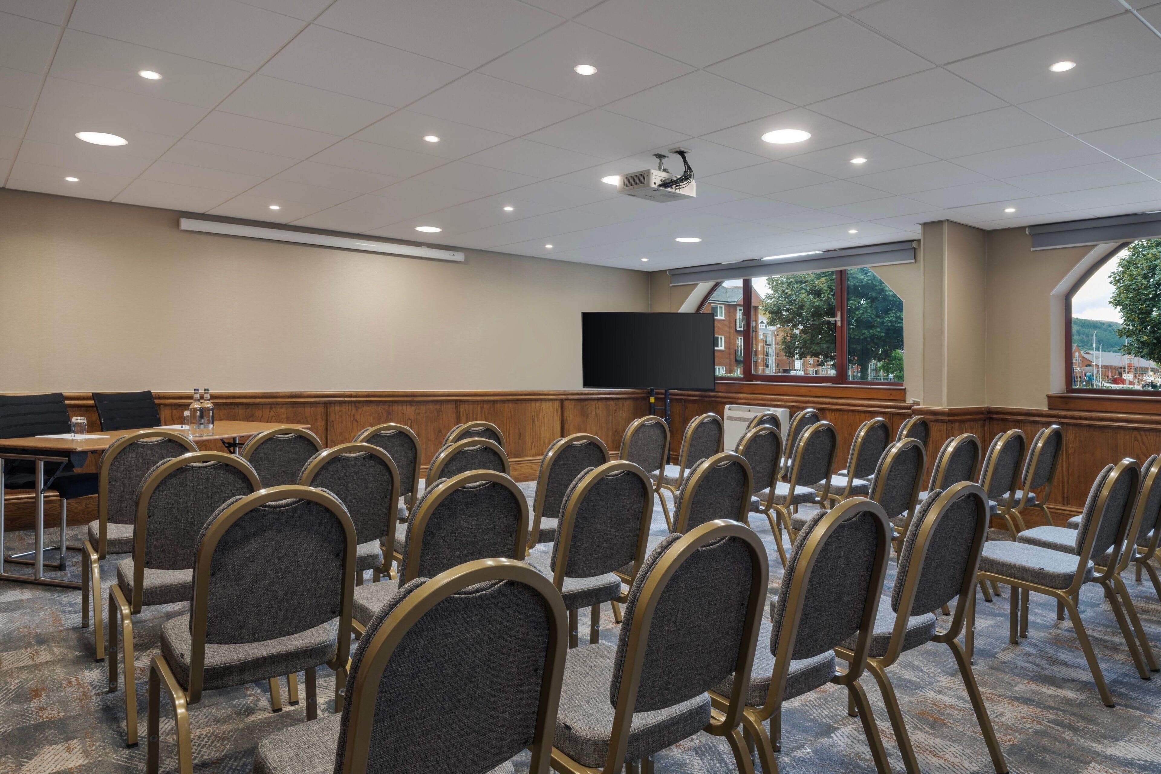 A conference room with rows of chairs, a large screen, and a projector on the ceiling.