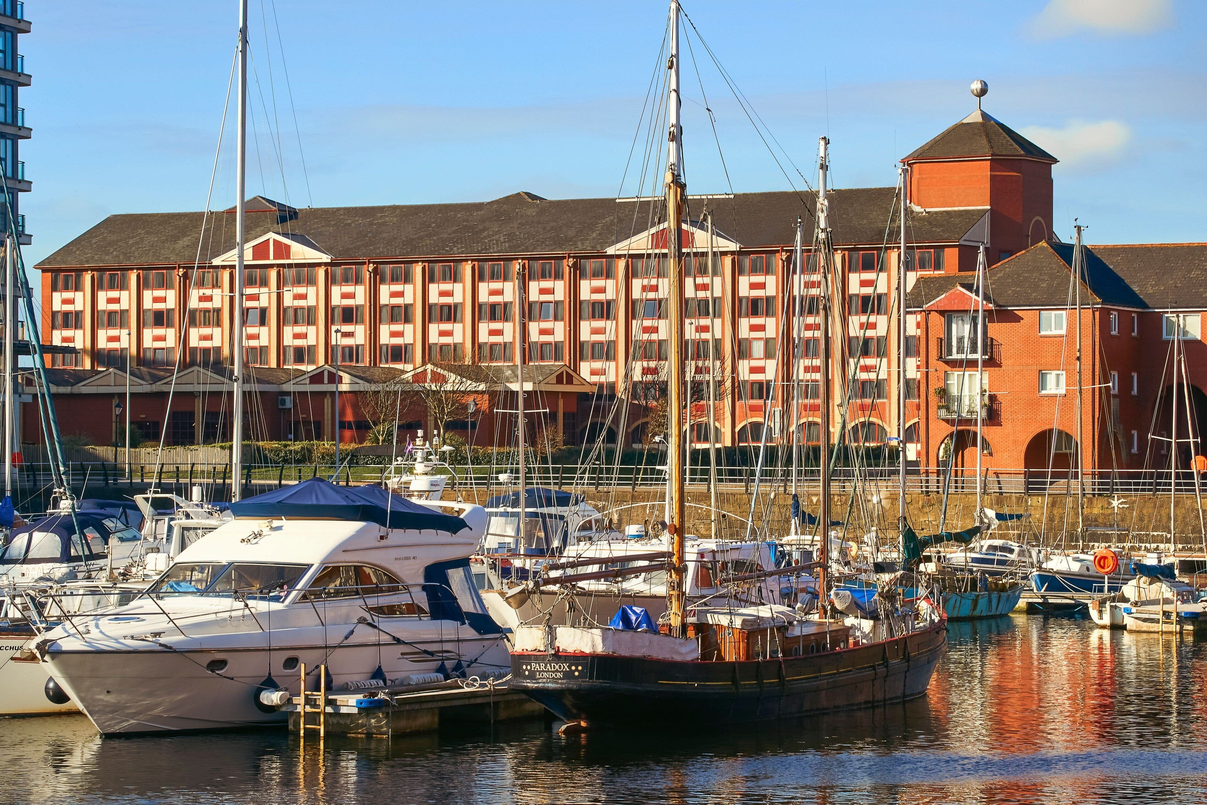 A marina with boats docked in front of a large red building with multiple windows and a tower.