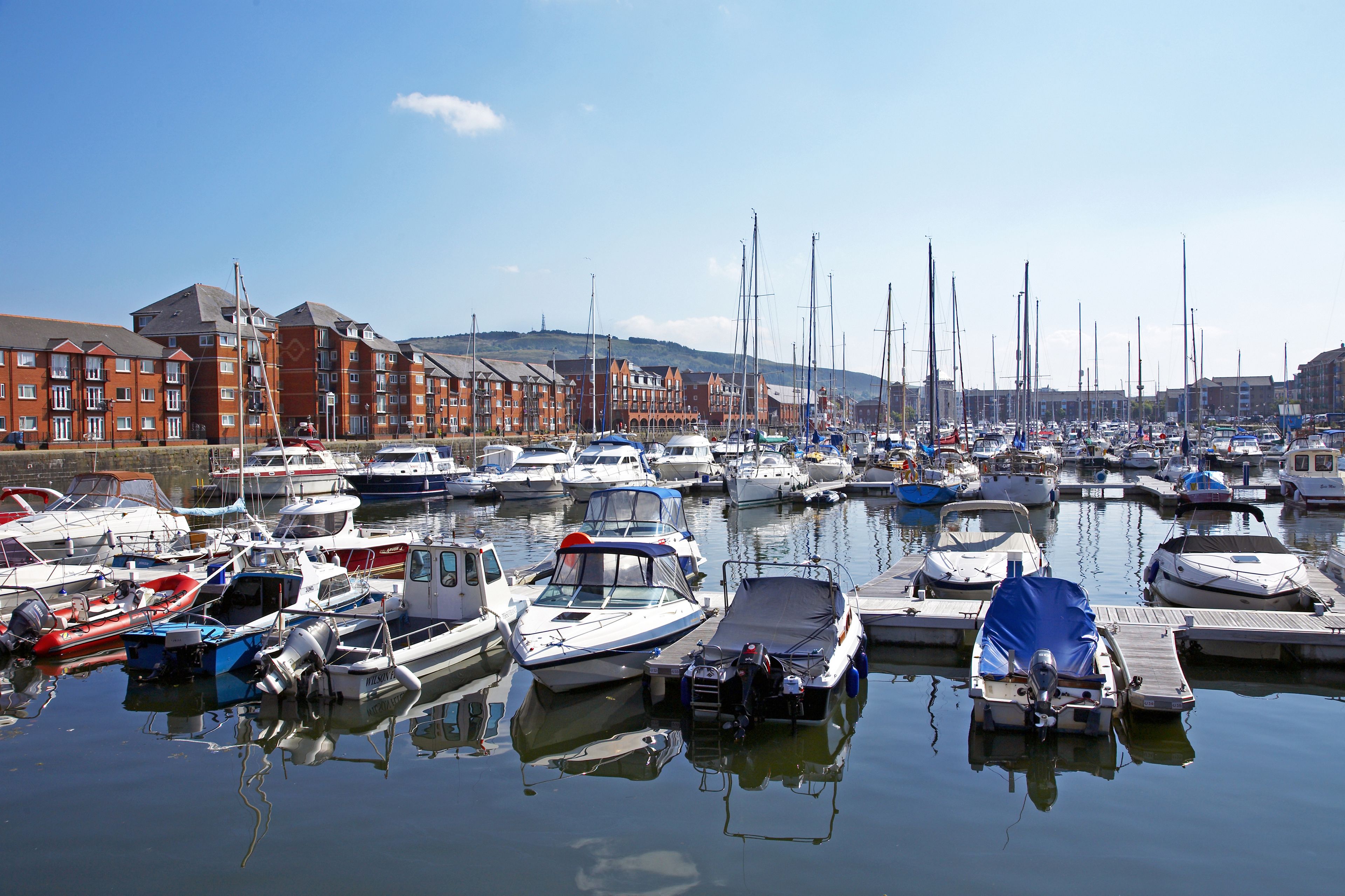 Un port de plaisance où sont amarrés différents types de bateaux, entouré d’immeubles.