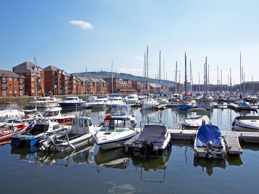 Un port de plaisance où sont amarrés différents types de bateaux, entouré d’immeubles.