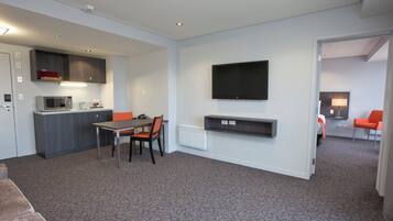 Una habitación de hotel moderna con kitchenette, un comedor, un televisor montado en la pared y una zona de estar con sofá y sillones.