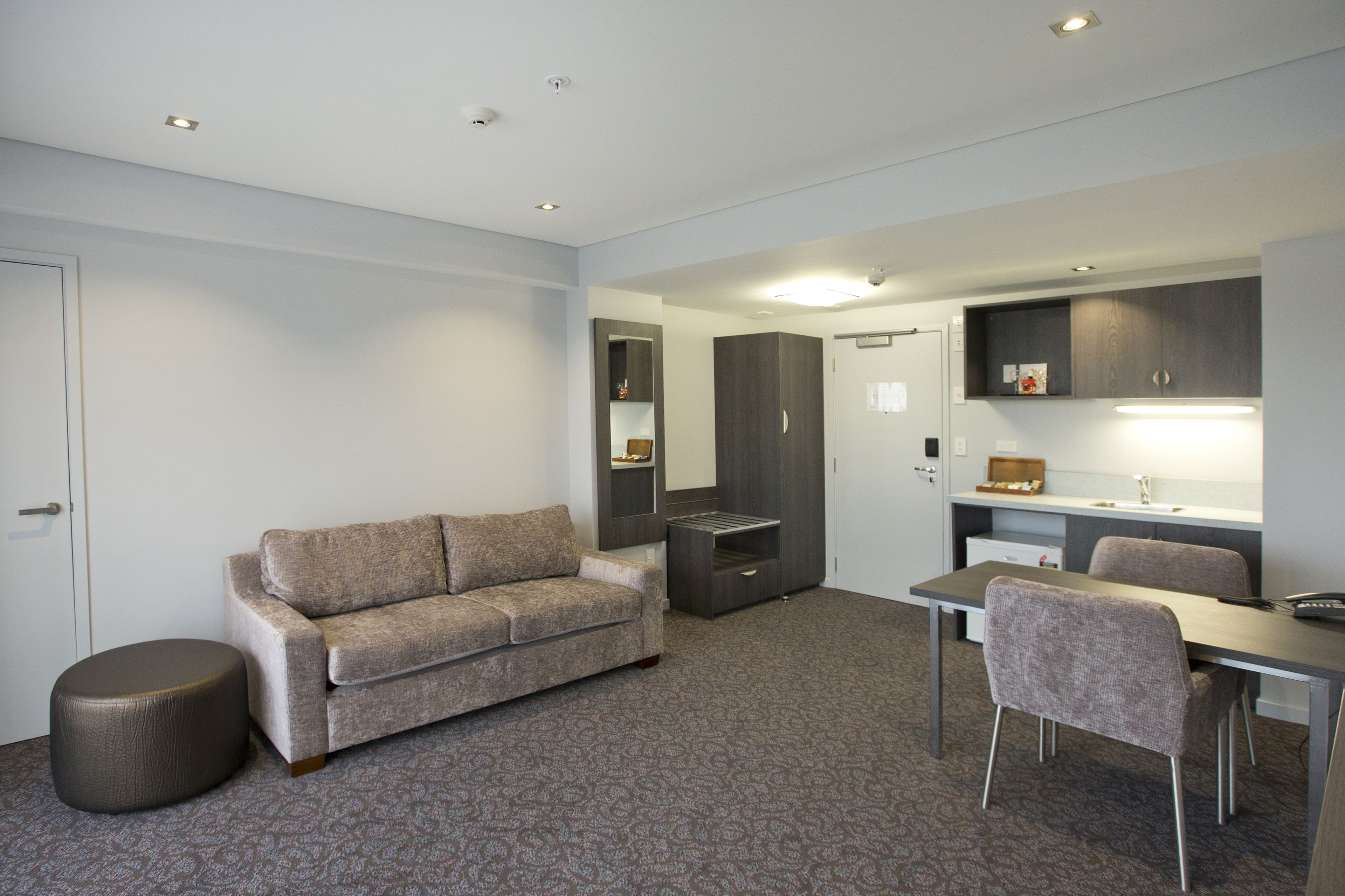 Ein modernes Hotelzimmer mit Sofa, Hocker, Esstisch und Stühlen.