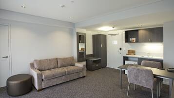 Ein modernes Hotelzimmer mit Sofa, Hocker, Esstisch und Stühlen.