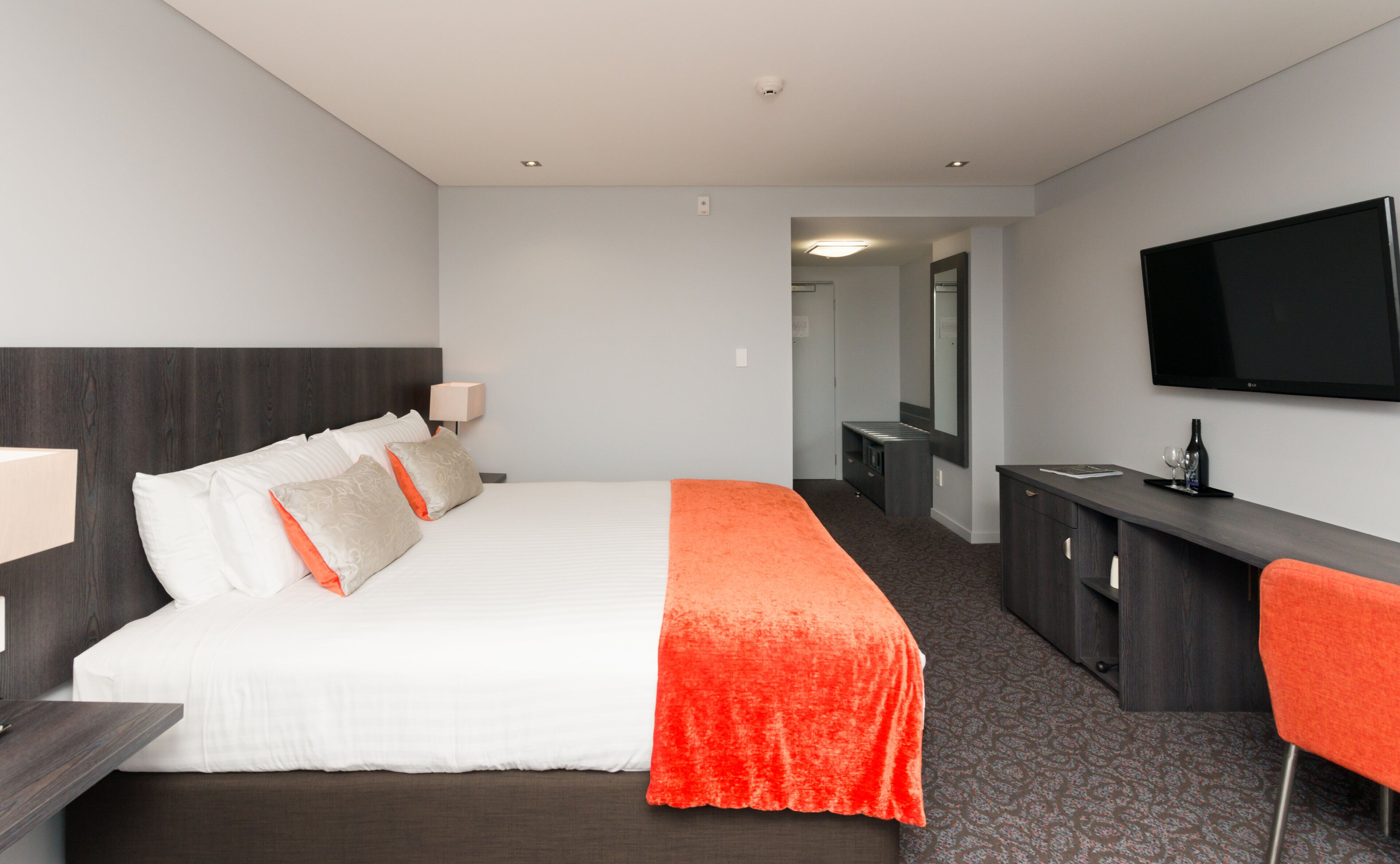 Een hotelkamer met een bed, bureau, televisie en spiegel.