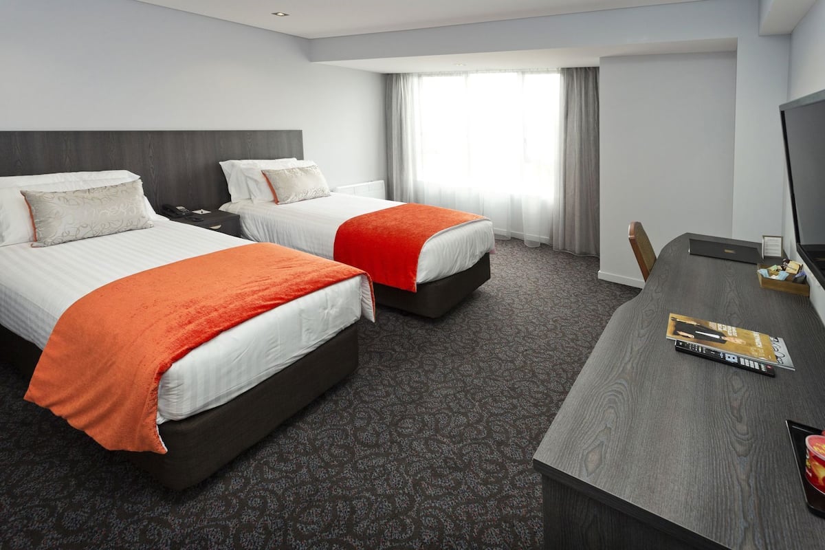 Ein Hotelzimmer mit zwei Betten, einem Schreibtisch und einem großen Fenster.