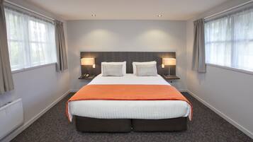 A large bed with an orange blanket, two bedside tables with lamps, and a headboard.