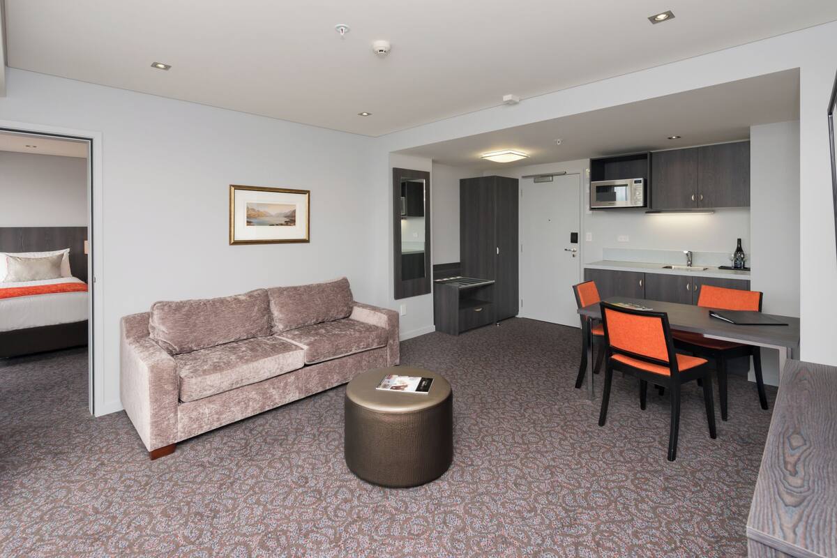 Ein modernes Hotelzimmer mit Bett, einer Couch, einem kleinen runden Tisch, einem Essbereich mit Stühlen und einer Küchenzeile.