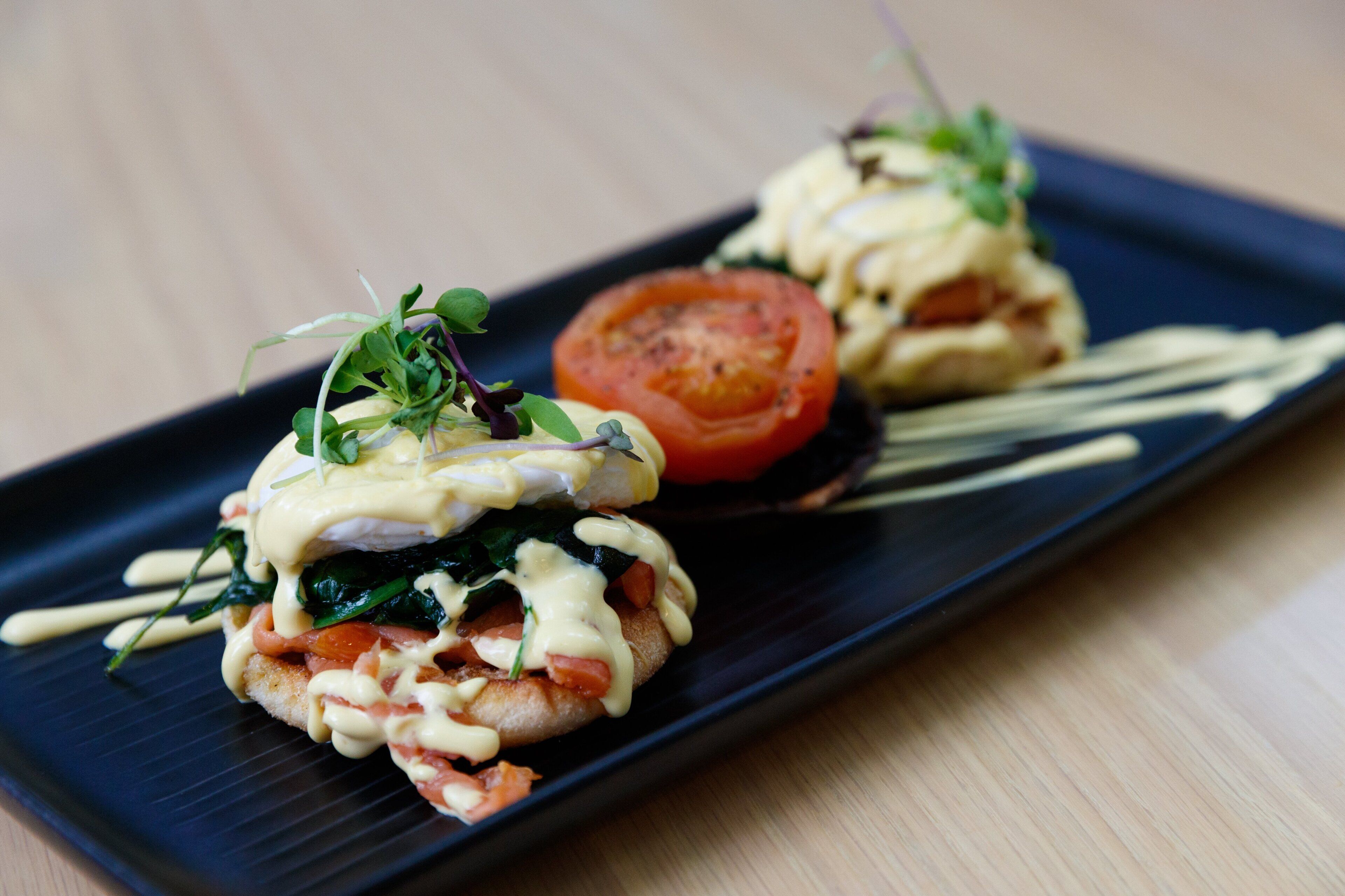 A black rectangular plate with two egg sandwiches garnished with greens and a slice of tomato.