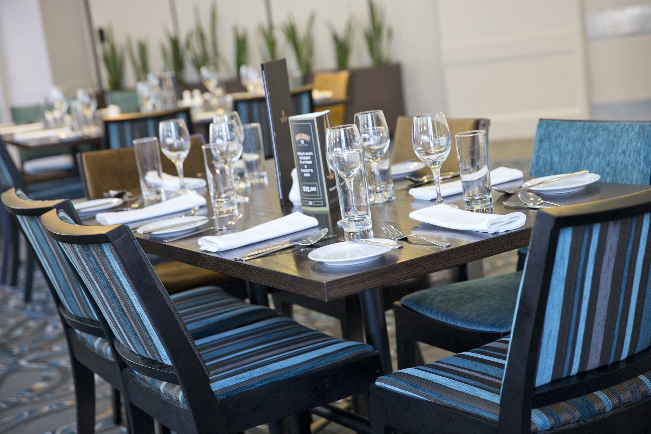 Un comedor con mesas dispuestas para el servicio, sillas con tapicería a rayas y un atril para el menú.