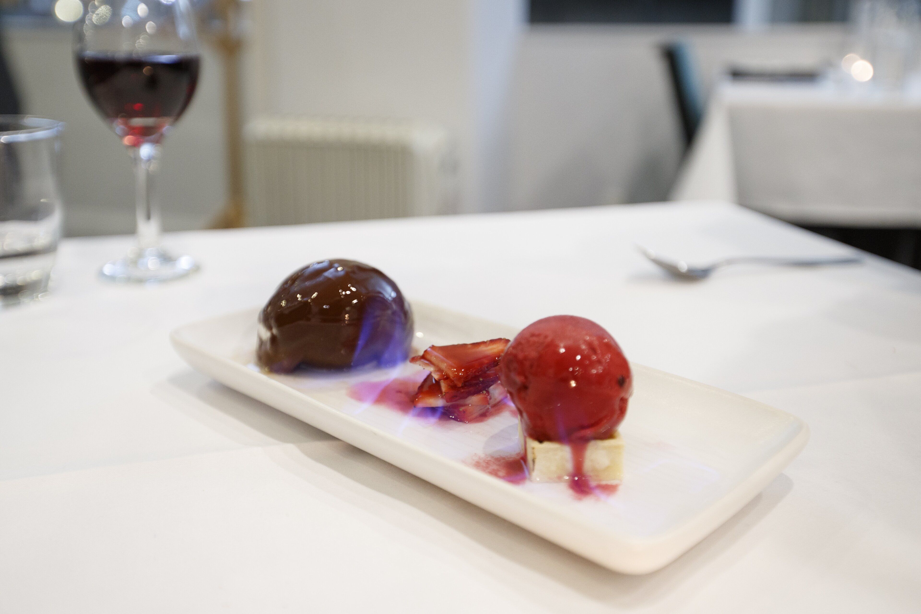 Une assiette à dessert avec deux boules de glace et une sphère de chocolat, le tout présenté sur une assiette rectangulaire blanche.