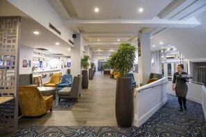 Eine Hotellobby mit Sitzbereichen, einem Empfangsschalter und einer großen Pflanze.