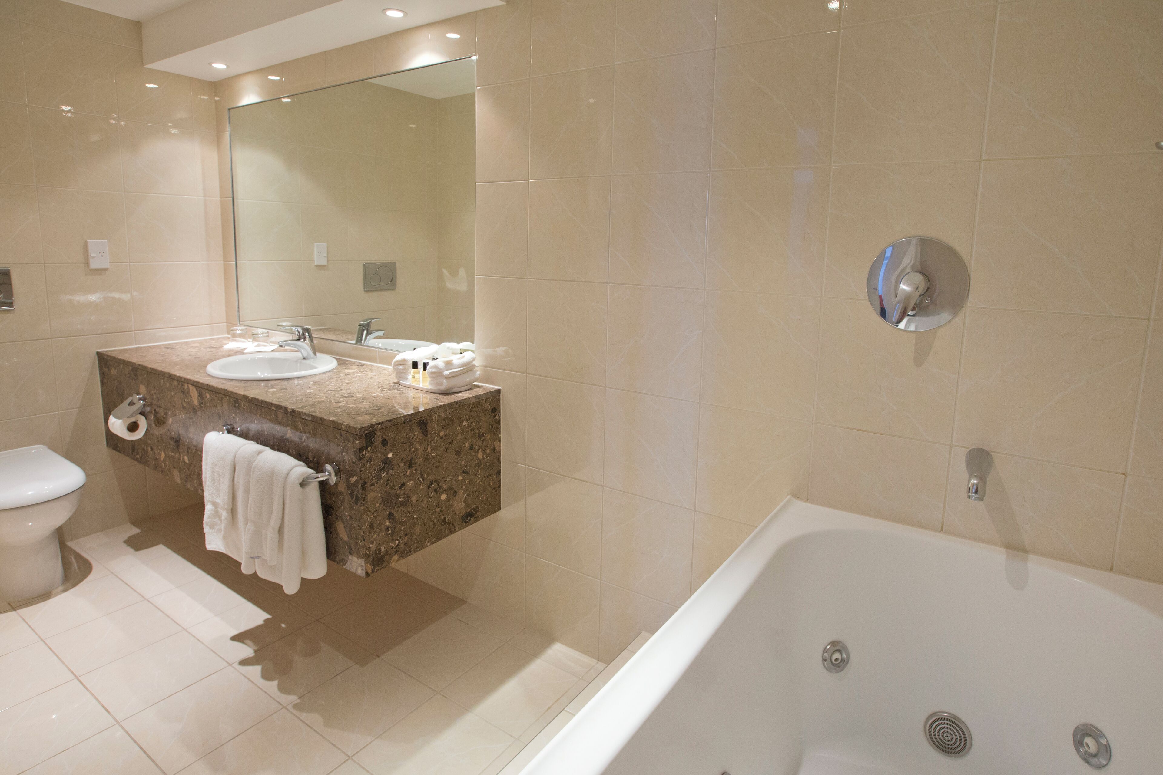 A modern bathroom with a marble sink, a large mirror, a toilet, and a bathtub.