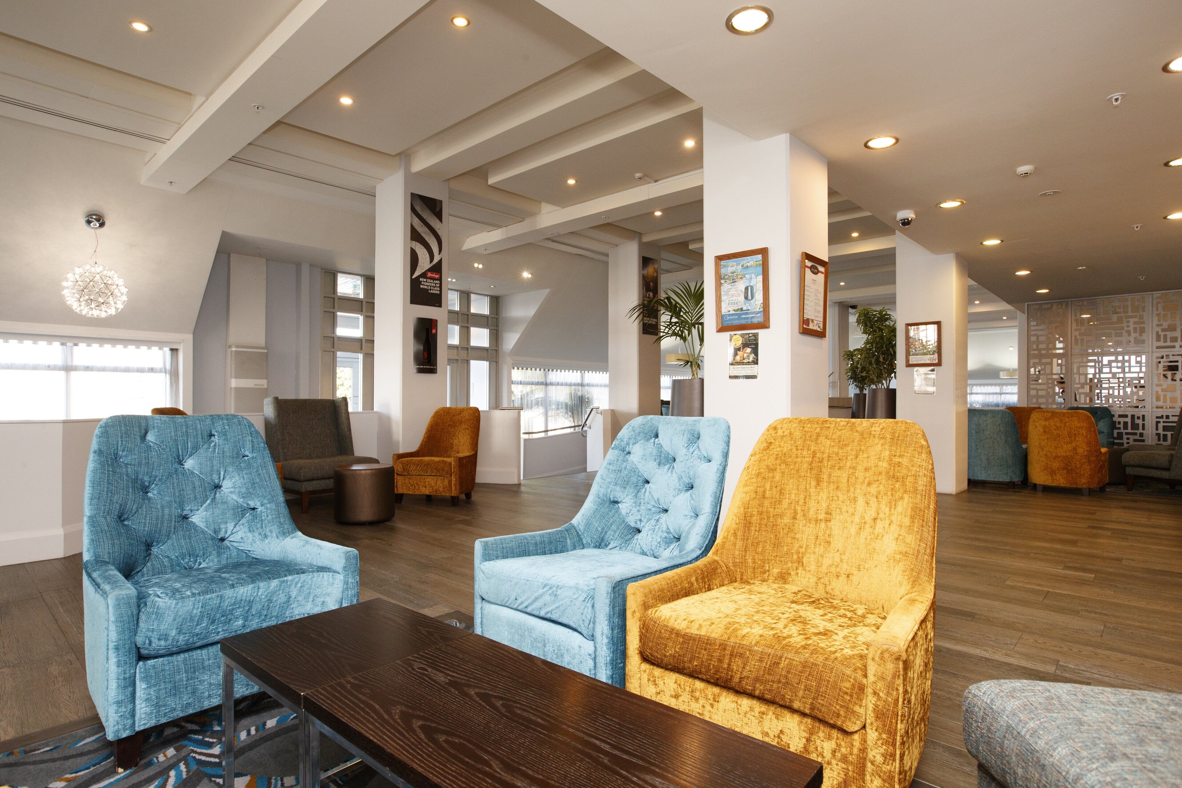 Un vestíbulo amplio con arreglos de asientos modernos, incluyendo sillones capitonados y sofás, una mesa de centro de madera y un adorno en la pared.
