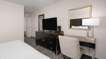 Habitación de hotel con cama, escritorio y silla, televisión, cafetera y espejo.