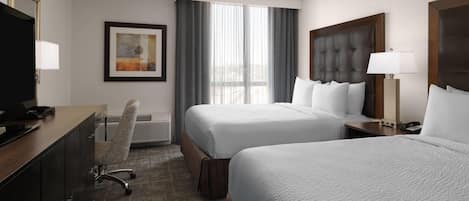A hotel room with two beds, a desk with a TV, a chair, a framed picture, and a window with curtains.