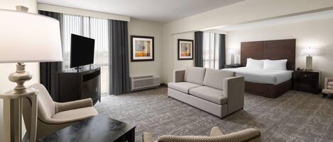 A hotel room with a bed, a sofa, a TV, a desk, and a chair.