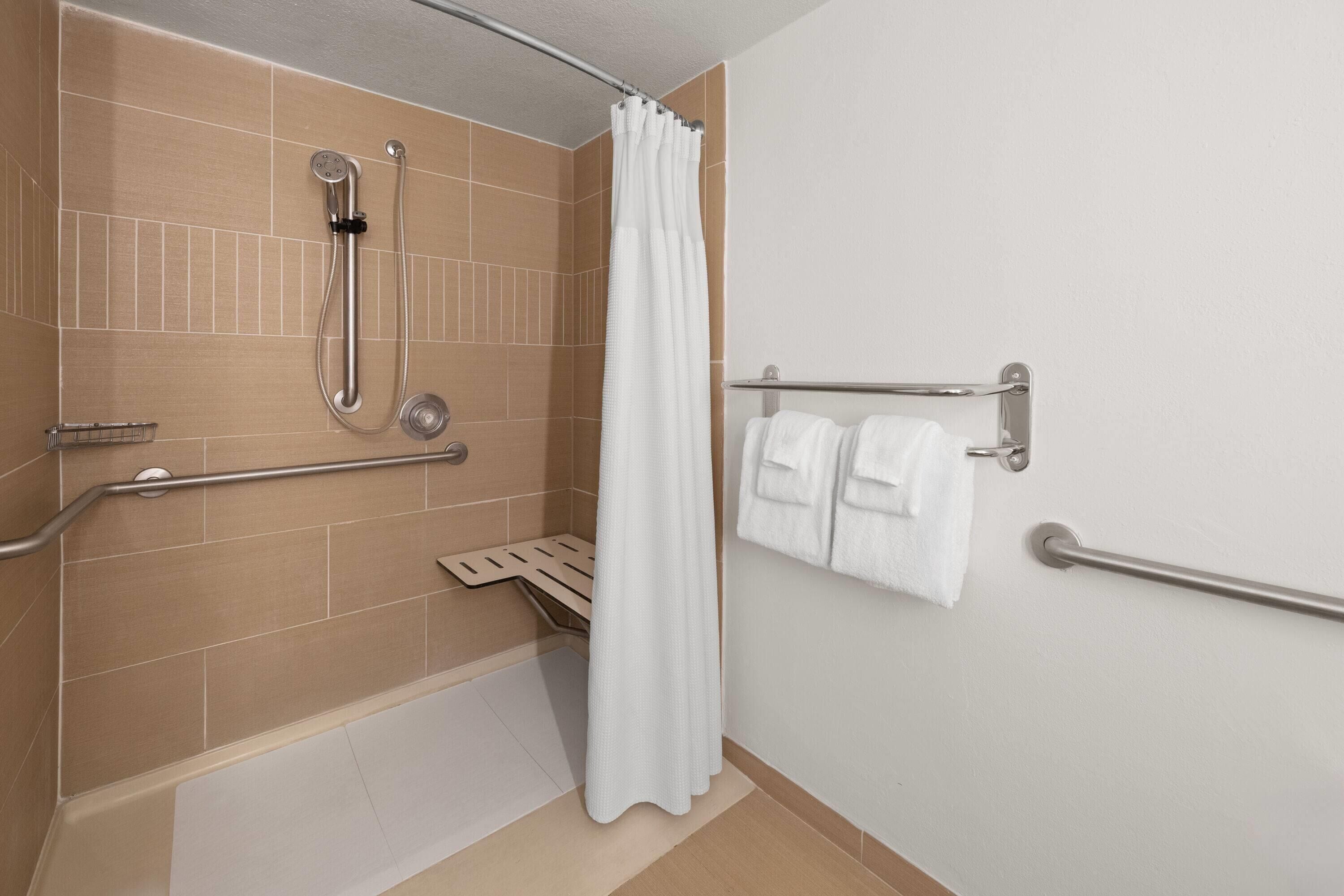 A bathroom with a shower, grab bars, a towel rack, and a white shower curtain.