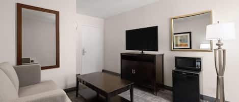 Habitación de hotel con sofá, televisión, un mueble bajo, microondas y lámpara.