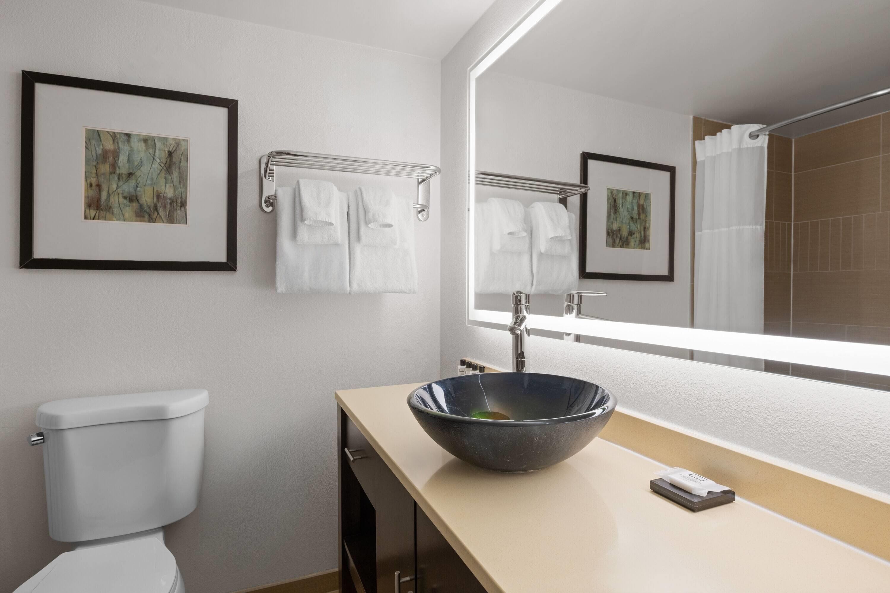A modern bathroom with a toilet, a sink with a large mirror, and two framed pictures on the wall.
