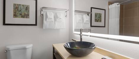 Un baño moderno con inodoro, lavamanos con un espejo grande y dos cuadros enmarcados en la pared.
