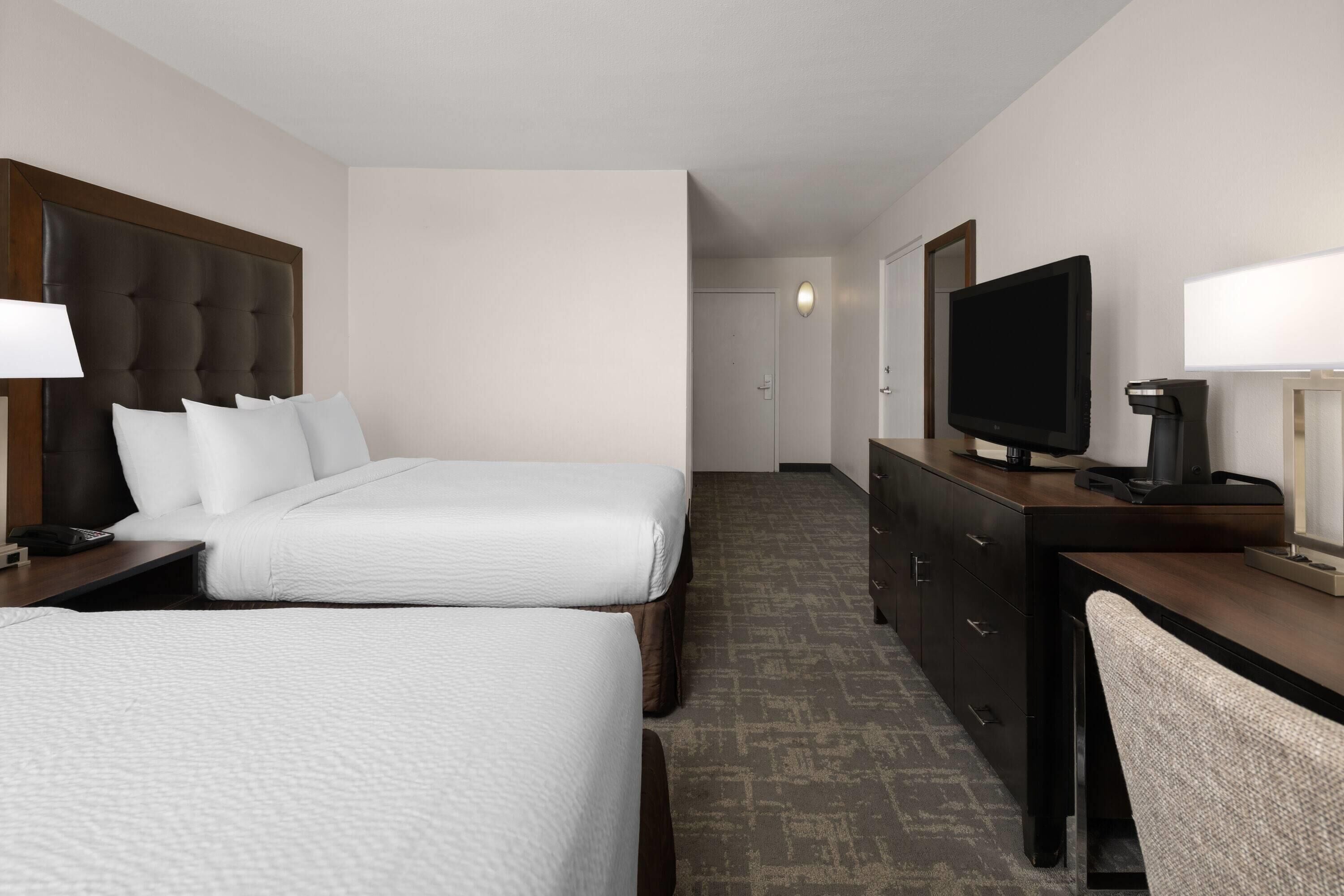 Een hotelkamer met twee bedden, een televisie, een bureau met lamp en een dressoir.