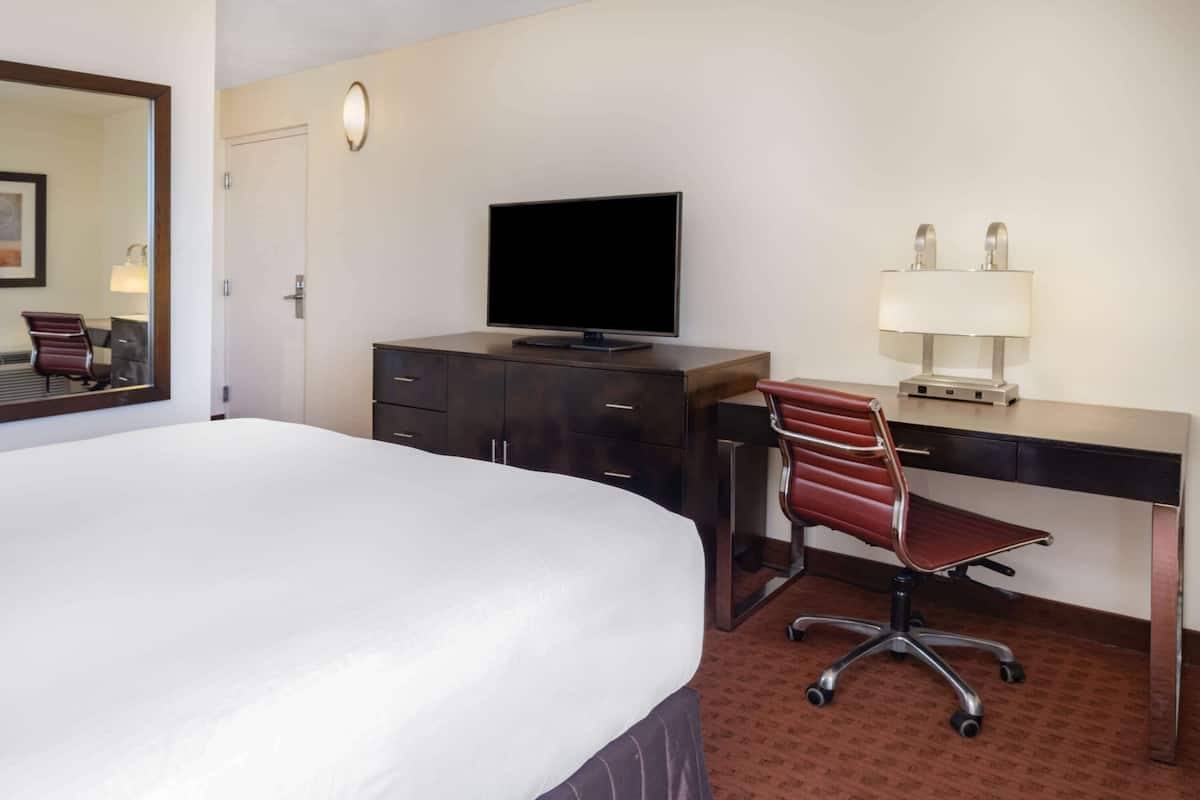 A hotel room with a large bed, a desk with a computer, a chair, a television, and a lamp.