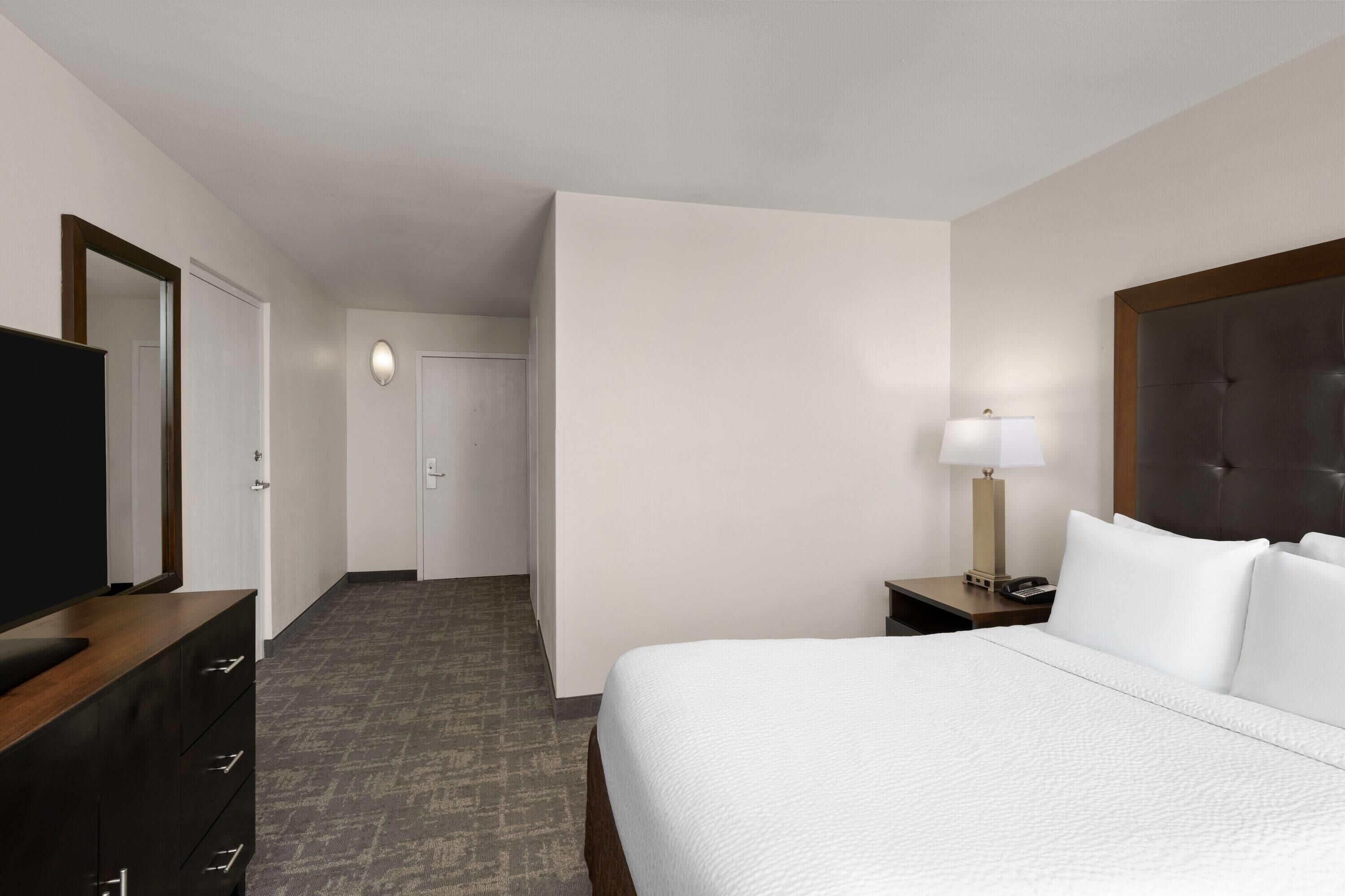 Habitación de hotel con cama, escritorio con lámpara, televisión y armario.