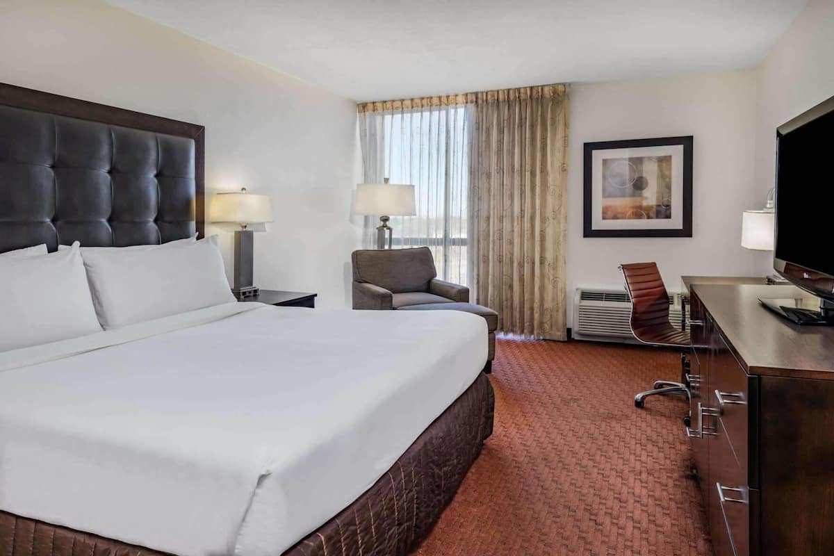 A hotel room with a large bed, a desk with a flat-screen TV, a chair, a lamp, and a framed picture on the wall.