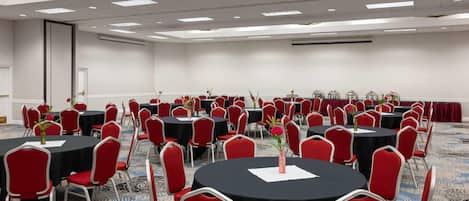 A conference room with multiple round tables, red chairs, and floral centerpieces.