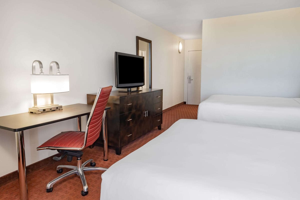 A hotel room with a desk, a chair, a television on a dresser, and two beds.