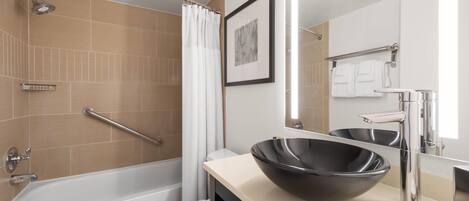 Un baño moderno con bañera, un espejo grande, un lavabo negro tipo cuenco y un inodoro.