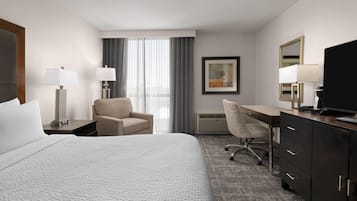 A hotel room with a bed, a desk, a chair, a television, and a window with curtains.