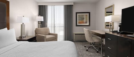 Ein Hotelzimmer mit Bett, Schreibtisch, Stuhl, Fernseher und einem Fenster mit Vorhängen.