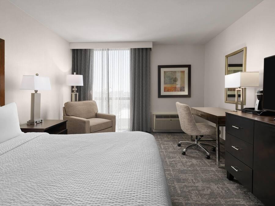 Een hotelkamer met een bed, een bureau, een stoel, een televisie en een raam met gordijnen.