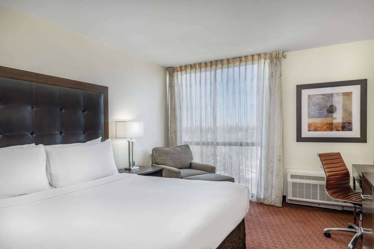 A hotel room with a large bed, a desk, a chair, and a window with curtains.