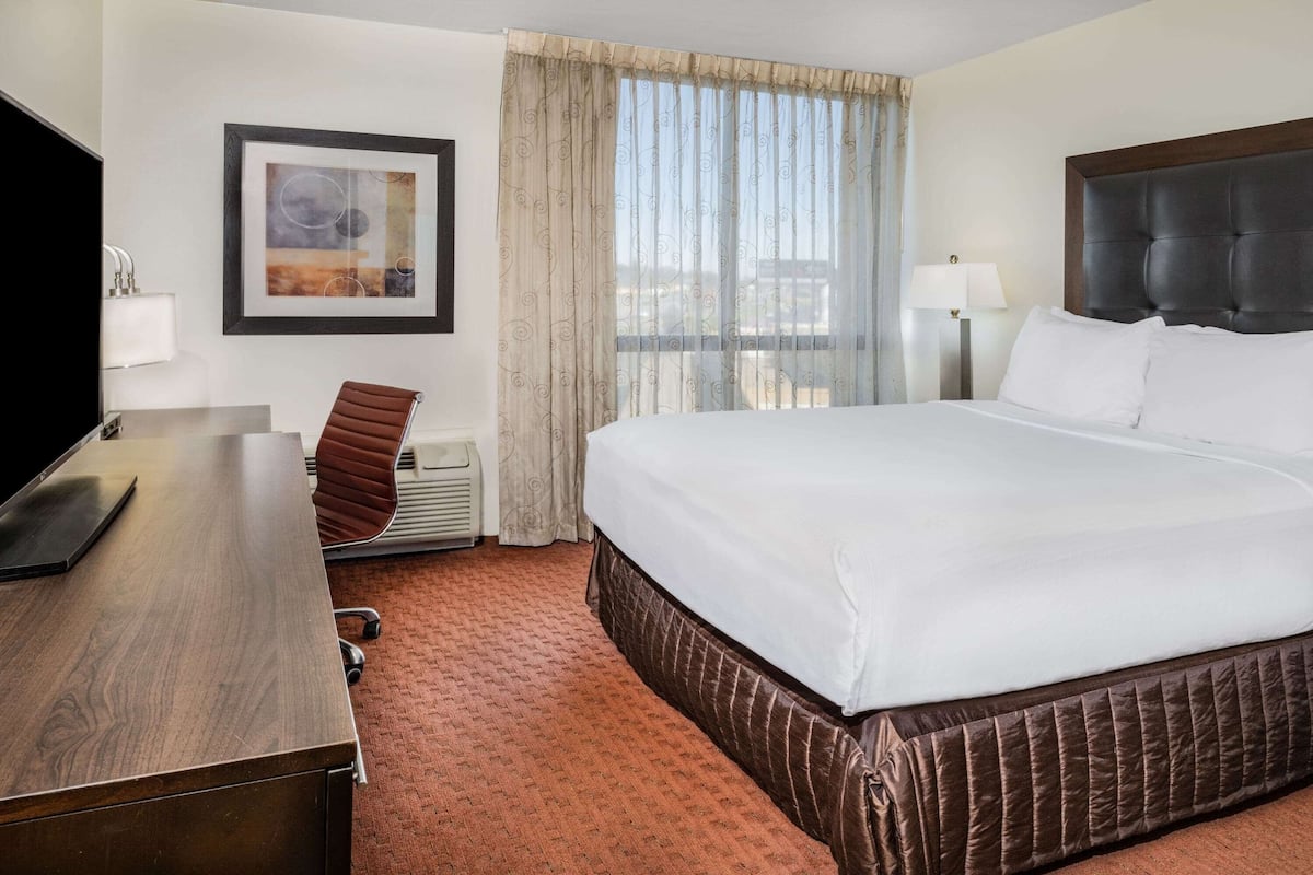 A hotel room with a large bed, a desk, a chair, a TV, and a window with curtains.