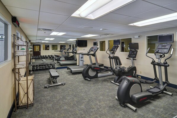 Une salle de sport équipée de tapis de course, de vélos elliptiques et d’haltères.