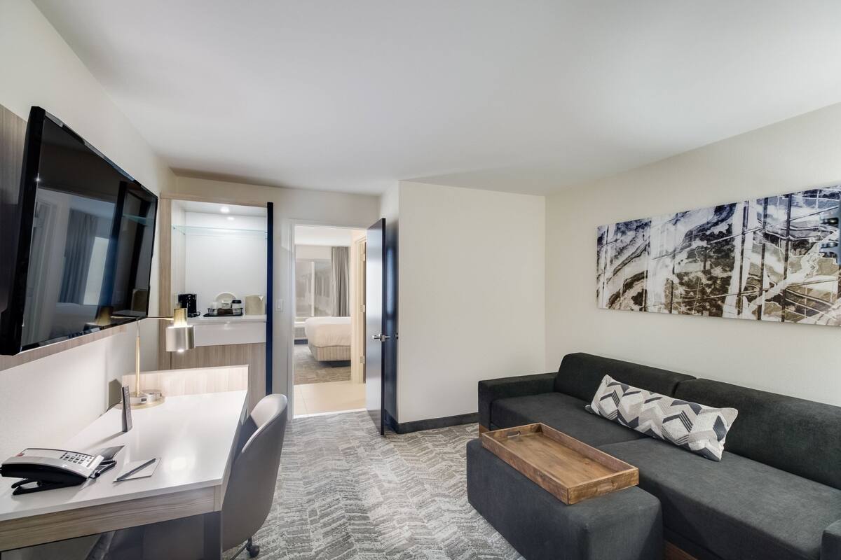 Una habitación de hotel moderna con escritorio, silla, sofá y un cuadro grande en la pared.