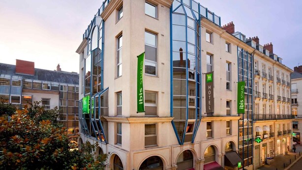 Un hôtel à plusieurs étages, doté d’une façade classique, de grandes fenêtres et d’une extension moderne en verre.